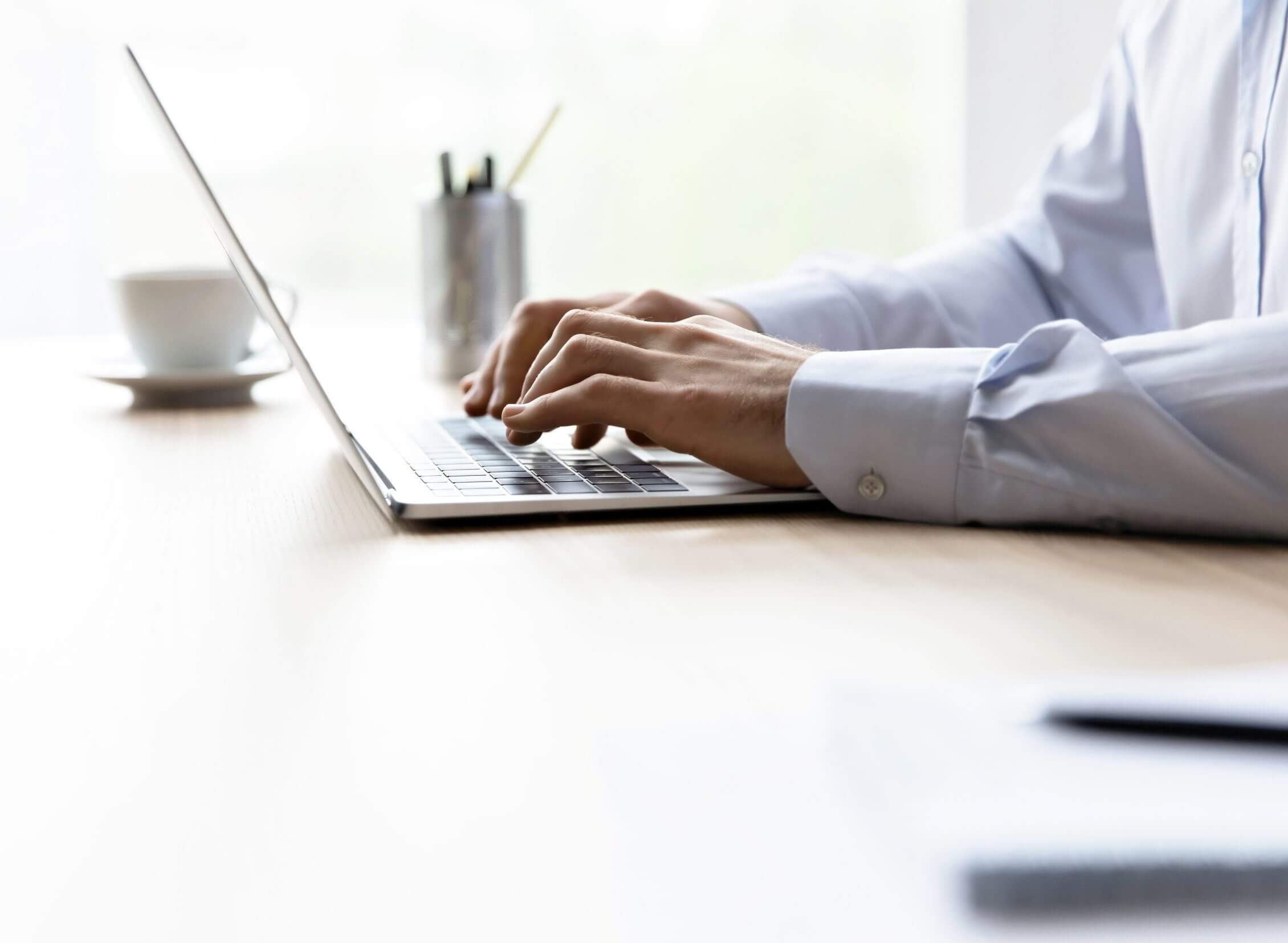 Hands of office employee typing on laptop keyboard at workplace